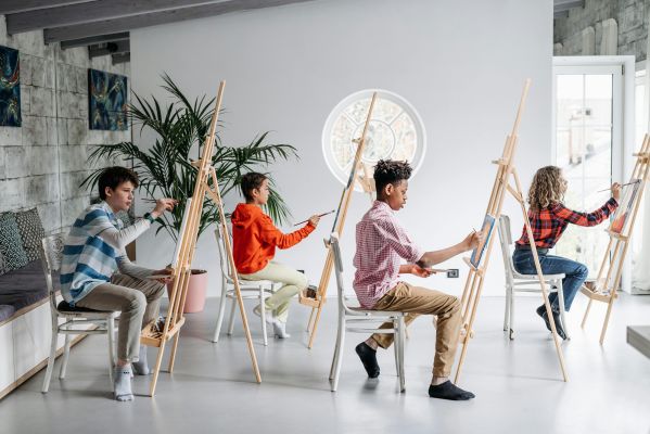 Young students focus on painting during an art class indoors, using easels.