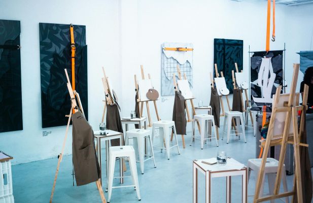Bright art studio filled with easels, aprons, and painting materials, ready for a class.